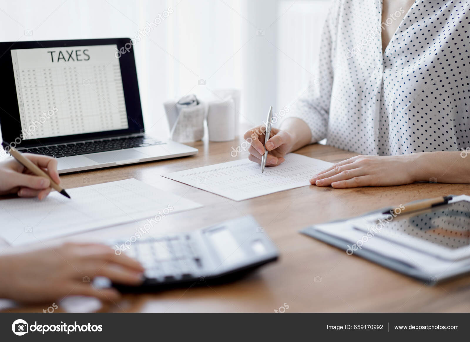 Two Accountants Using A Laptop Computer And Calculator While Counting Taxes At Wooden Desk In Office. Teamwork In Business Audit And Finance